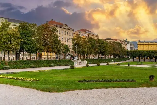 Vienna's Hofburg Palace gardens with manicured lawns, historic buildings, and tree-lined pathways at golden hour