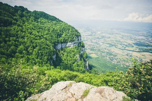 Vista desde un acantilado rocoso cerca de Annemasse, Francia, sobre una ladera montañosa verde y un amplio valle con campos y pequeños pueblos abajo.