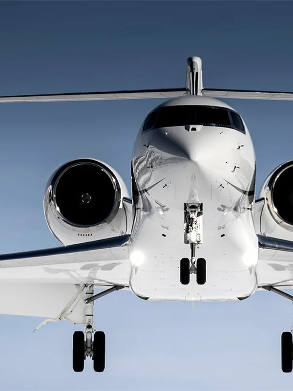 Frontalansicht eines Privatjets vom Boden aus, die zwei Triebwerke und das Bugfahrwerk vor blauem Himmel zeigt