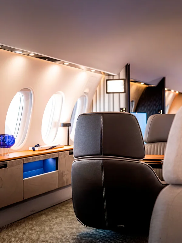 Modernes Privatjet-Interieur mit dunklen Ledersitzen, warmer Beleuchtung und Sideboard aus Holz und Marmor