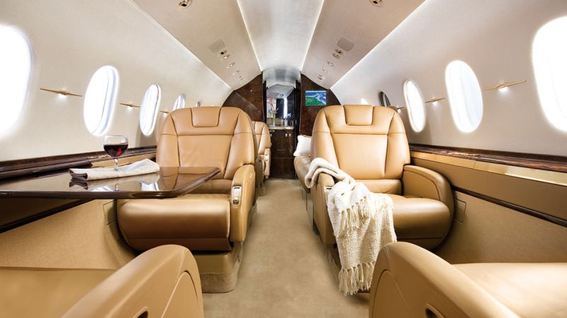 Interior cabin view of Hawker 4000 private jet showing tan leather seats, windows, and galley area with modern luxury furn...
