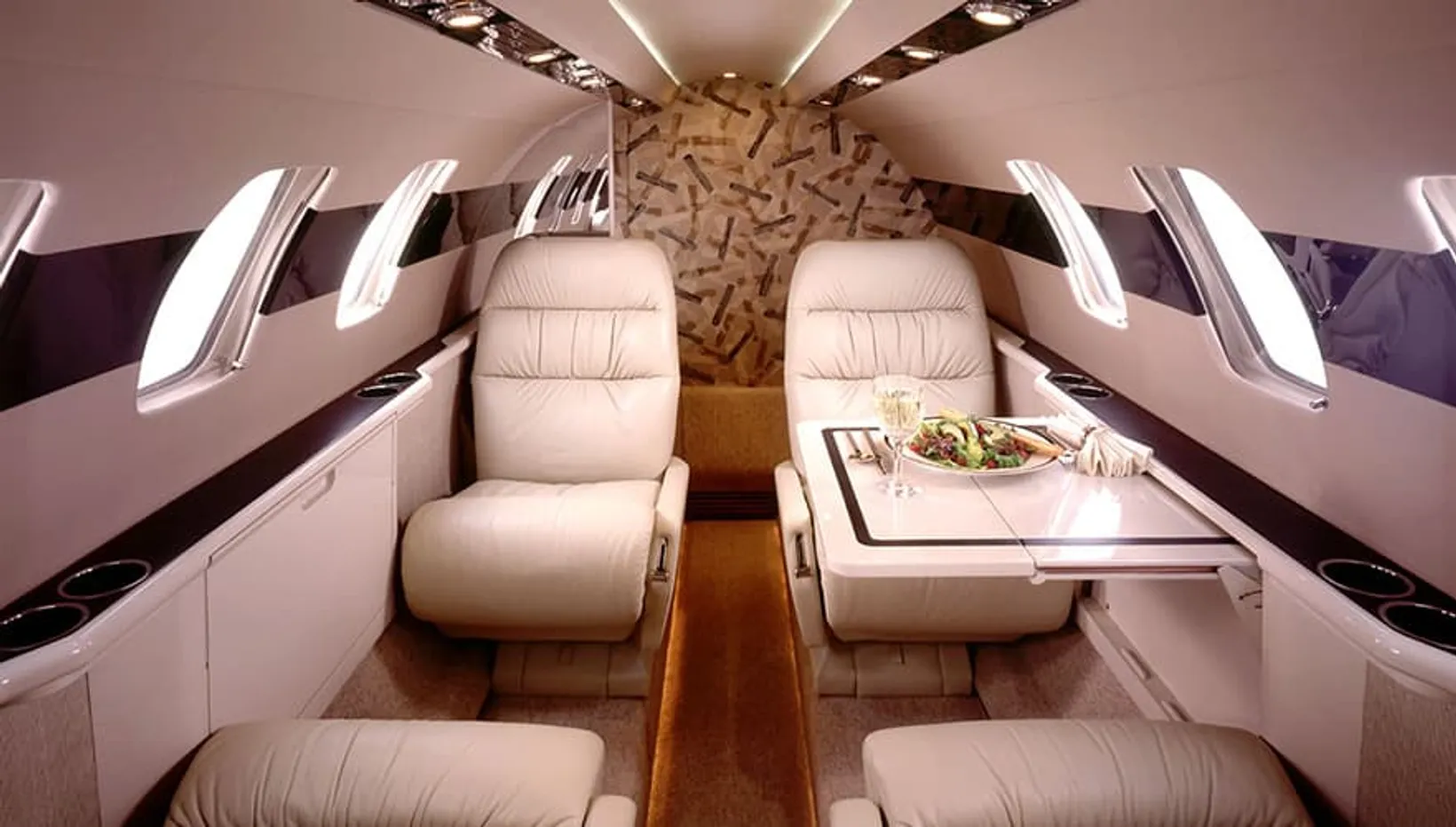 Luxurious cabin interior of a Cessna Citation CJ1 private jet with cream leather seats, wooden accents, and gourmet meal s...