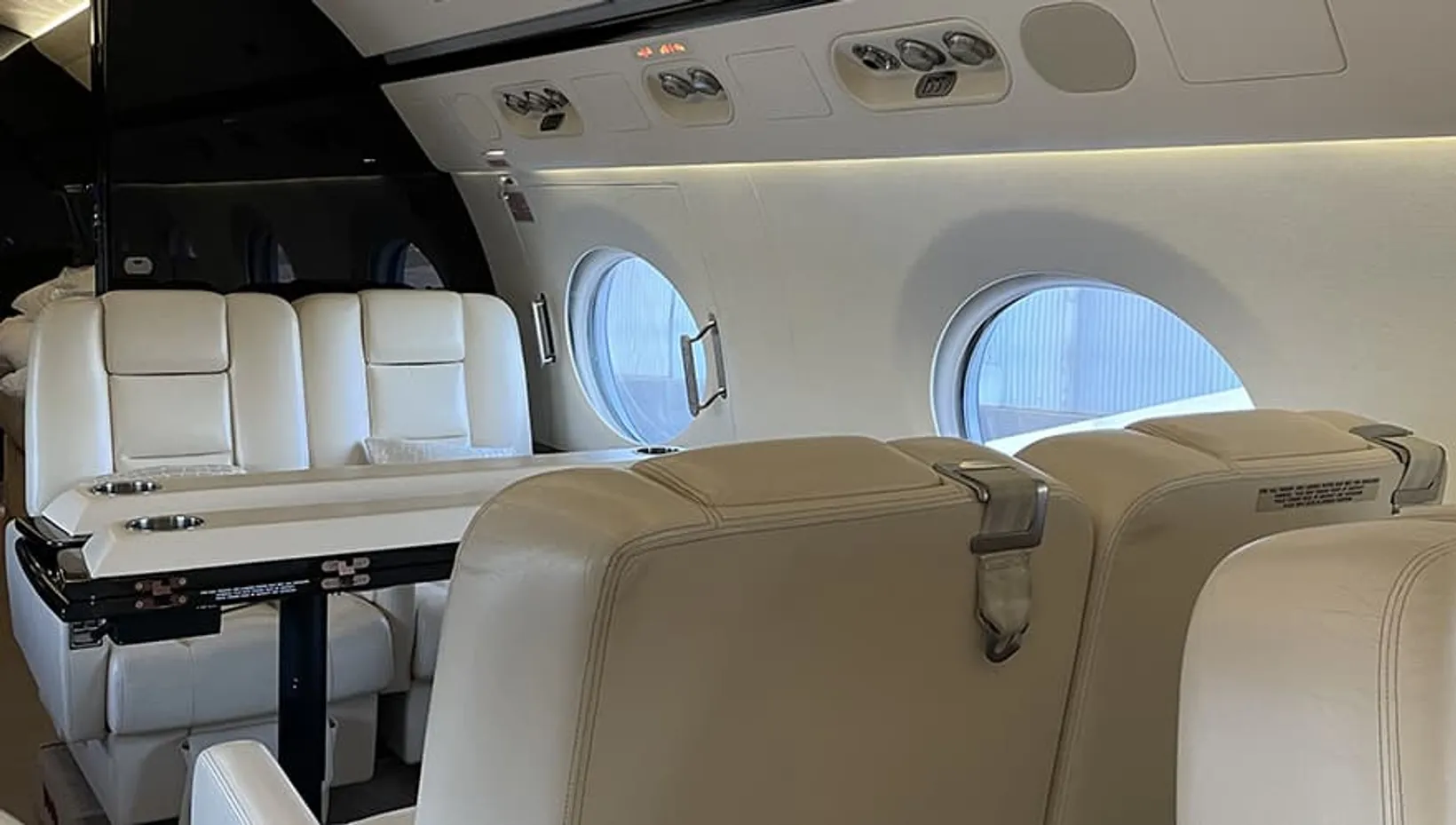 Interior cabin view of Bombardier Challenger 650 showing cream leather seats, oval windows, overhead ventilation panels, a...