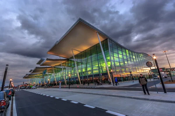 Nowoczesny terminal ze szkła i stali na lotnisku im. Mikołaja Kopernika we Wrocławiu oświetlony o zmierzchu na tle dramatycznego, zachmurzonego nieba.