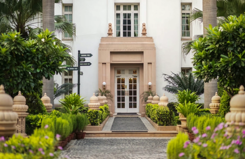 Garden path leading to a doorway at The Imperial hotel in New Delhi, framed by palms and flowering plants