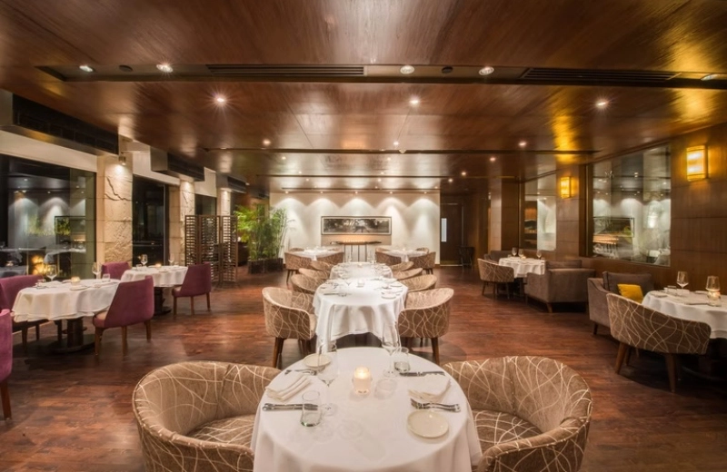Indian Accent dining room in New Delhi, with white tablecloths, upholstered chairs and warm wood finishes