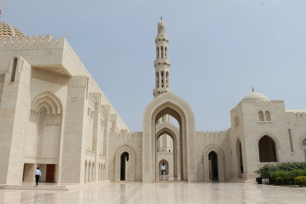 Sultan Qaboos Grand Mosque in Muscat, with ornate stone arches, a tall minaret and a marble courtyard.