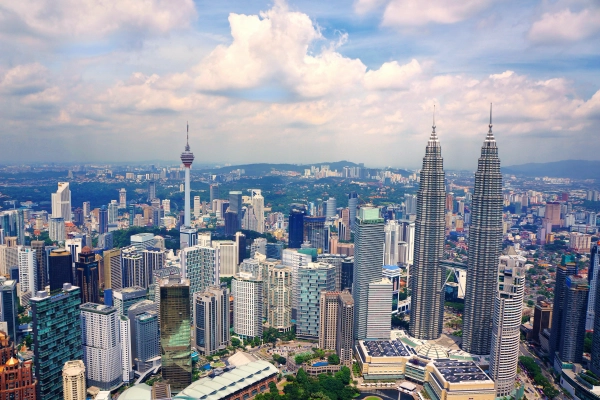 Kuala Lumpur skyline with the Petronas Twin Towers and KL Tower beneath a partly cloudy sky.
