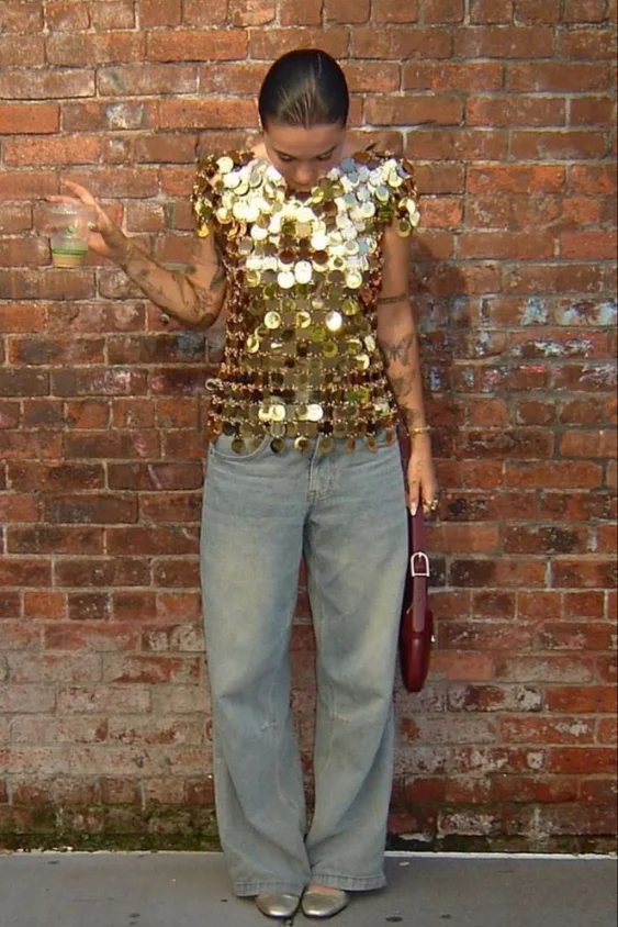 Woman wearing a vintage gold paillette top with light-wash jeans. Bold sparkle meets laid-back tailoring.