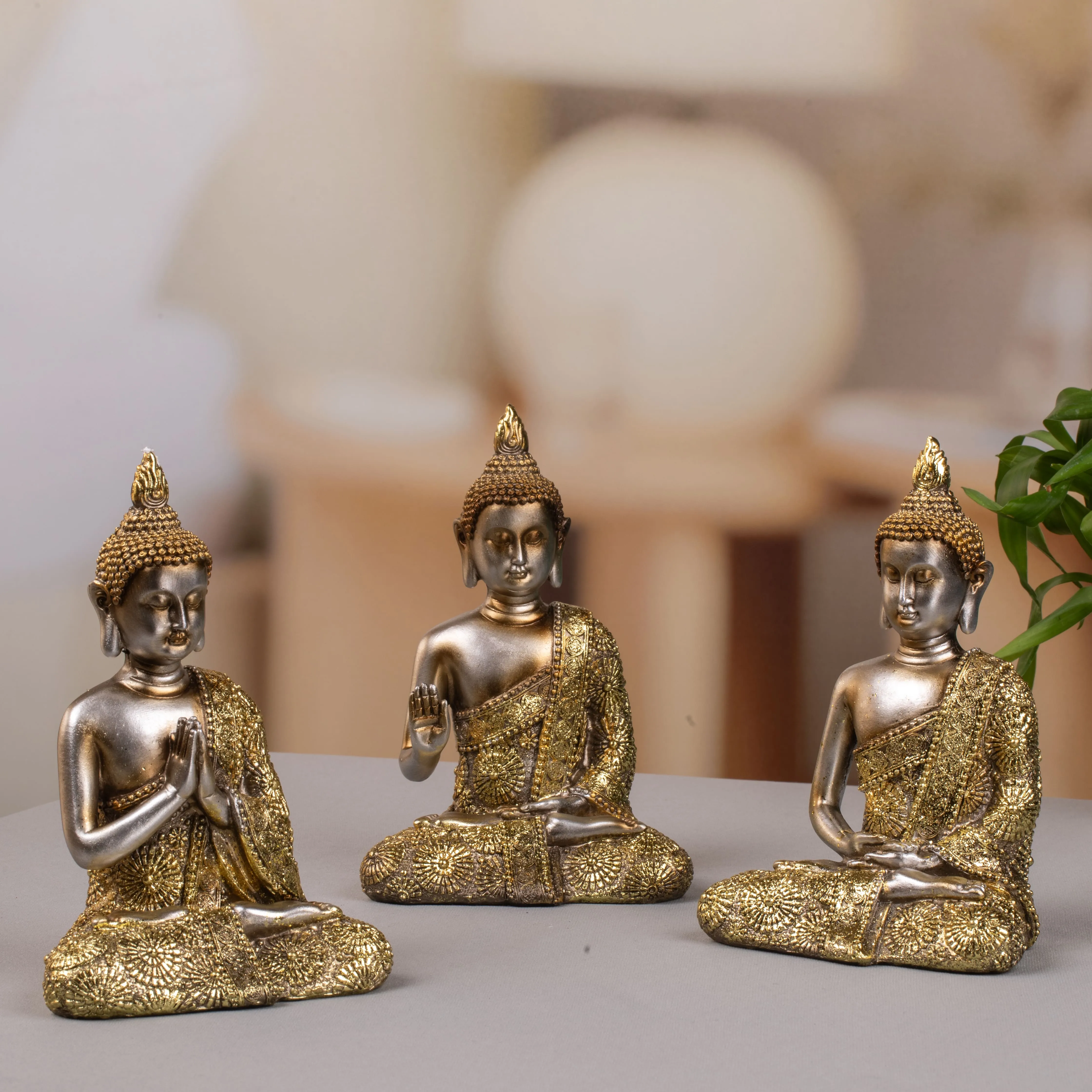 Three gold and bronze Buddha statues in different meditation poses on a gray surface with a blurred background.