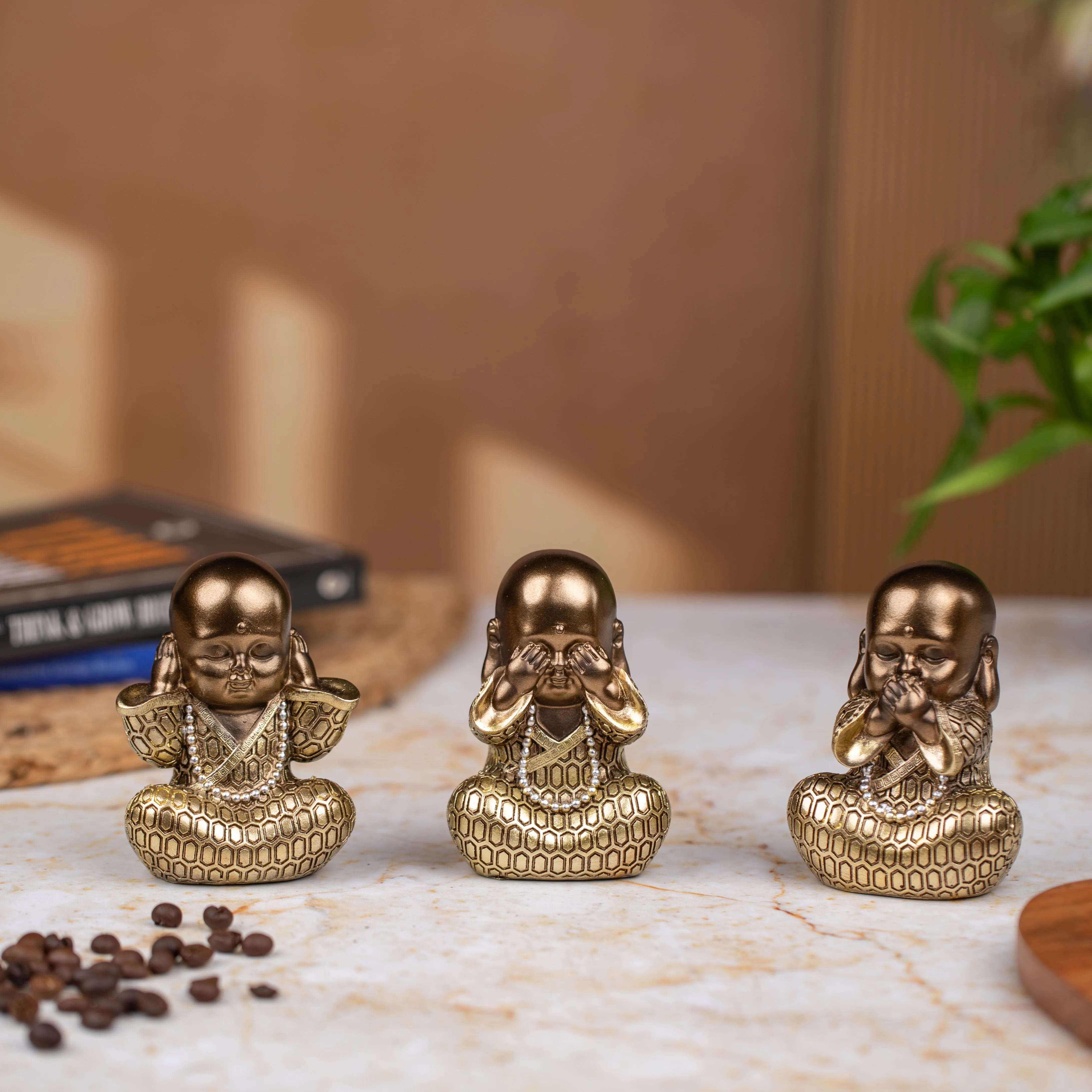 Three small golden statues of meditating monks in poses representing hear no evil, see no evil, and speak no evil on a marble surface.