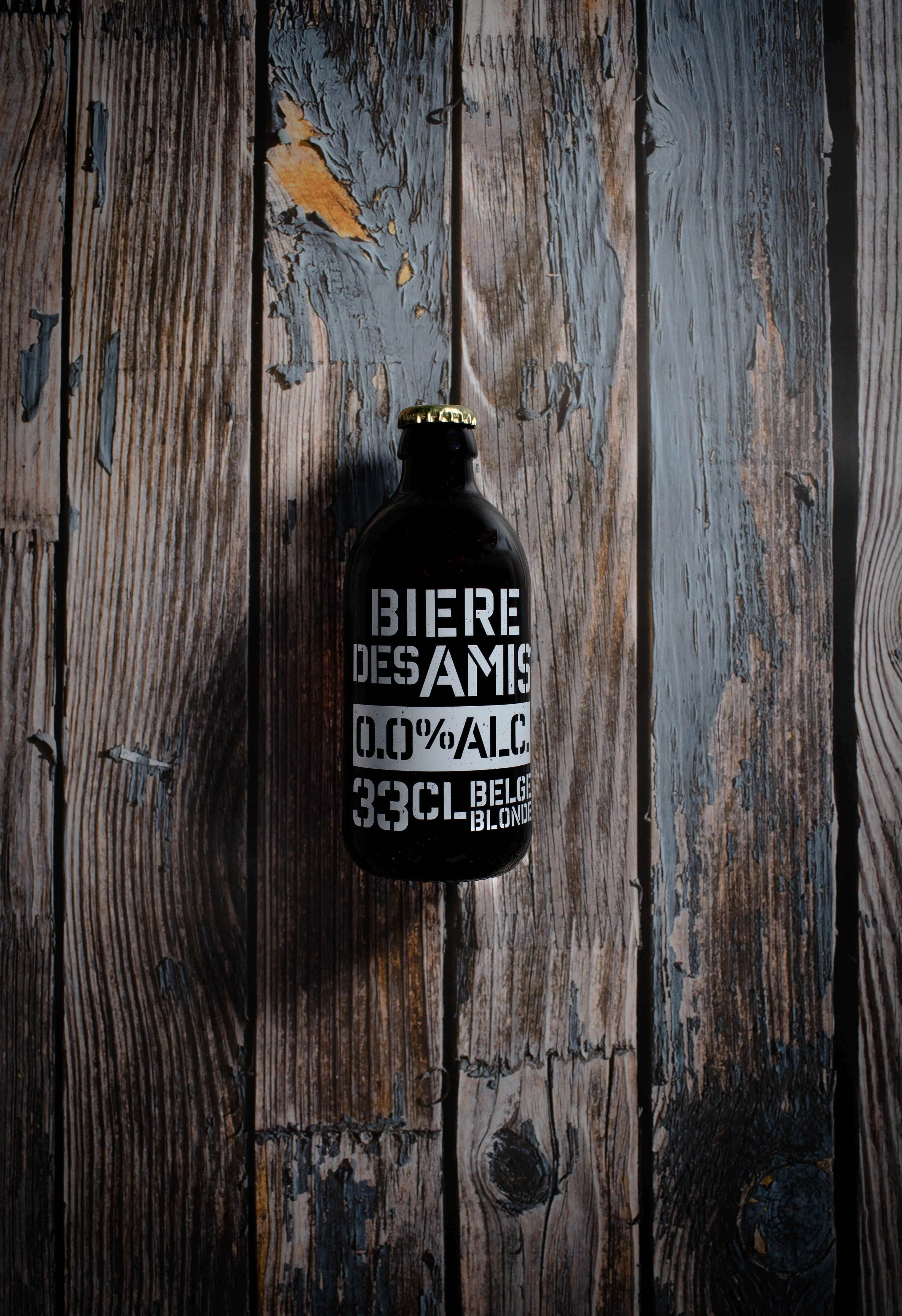 Dark bottle labeled 'Biere Des Amis 0.0% ALC 33CL Belgian Blonde' on weathered wooden surface.