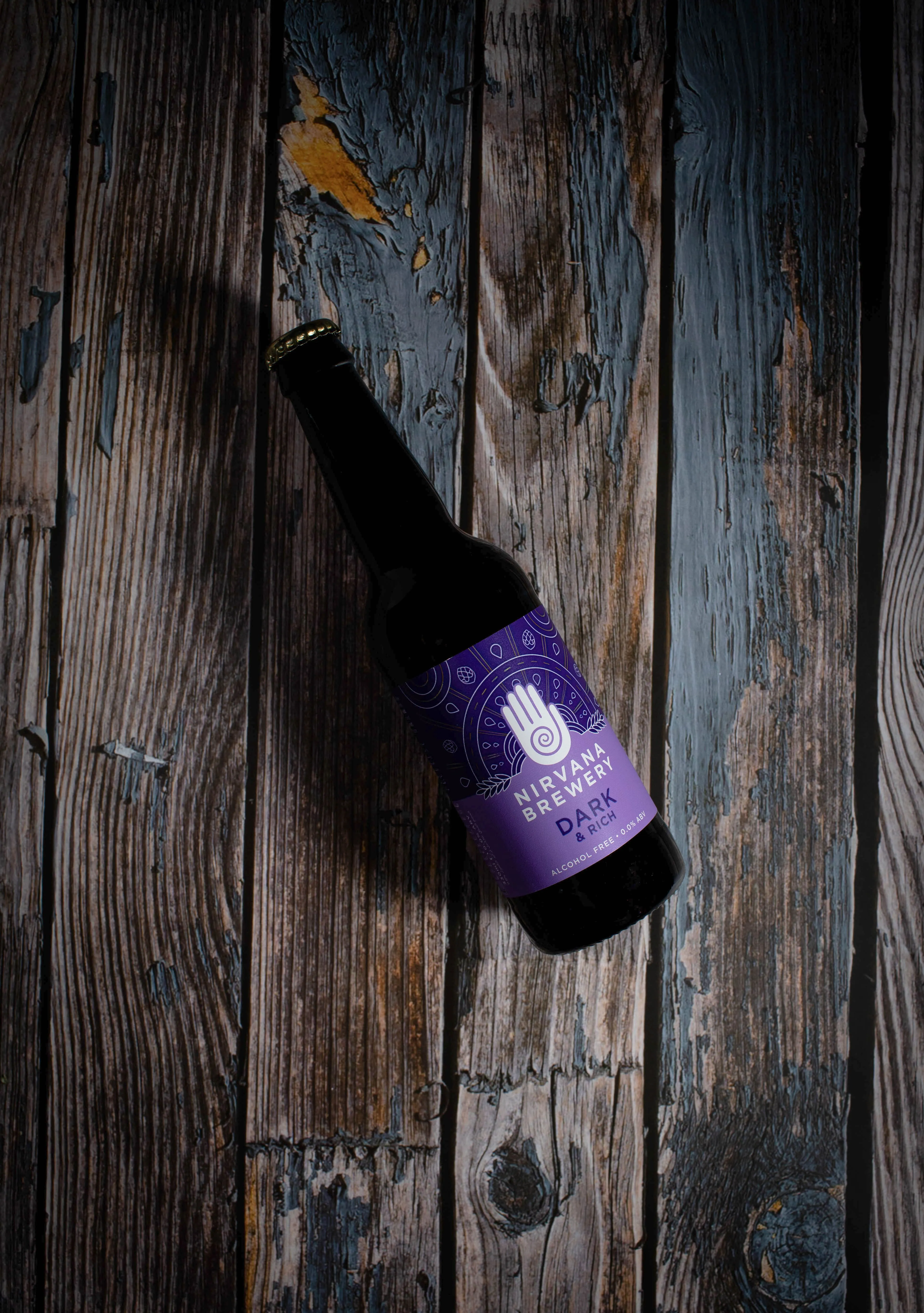 Dark beer bottle with a purple label reading Nirvana Brewery Dark & Rich on weathered wooden surface.