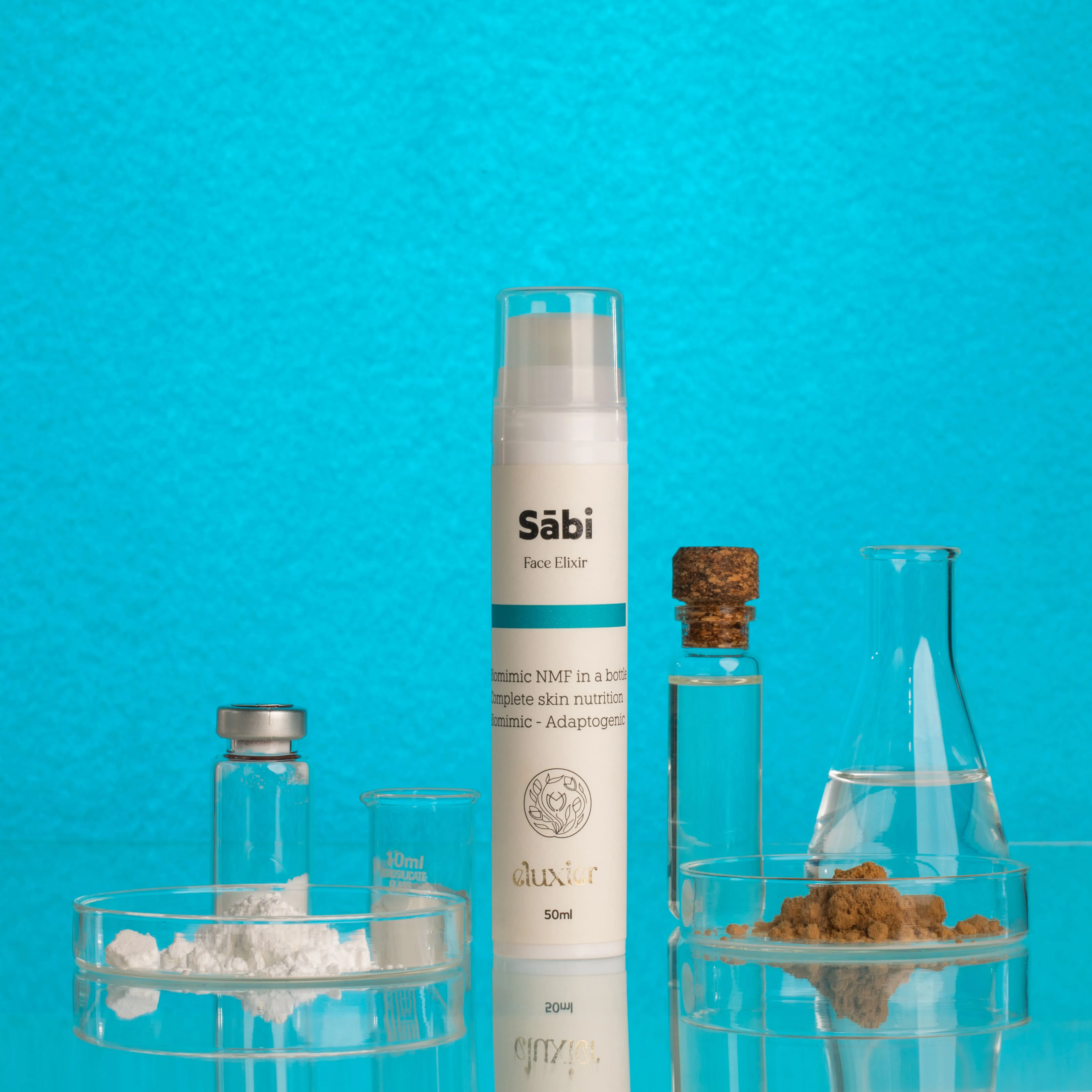 Säbi Face Elixir bottle surrounded by glass containers holding white powder, brown powder, and clear liquid against a blue background.