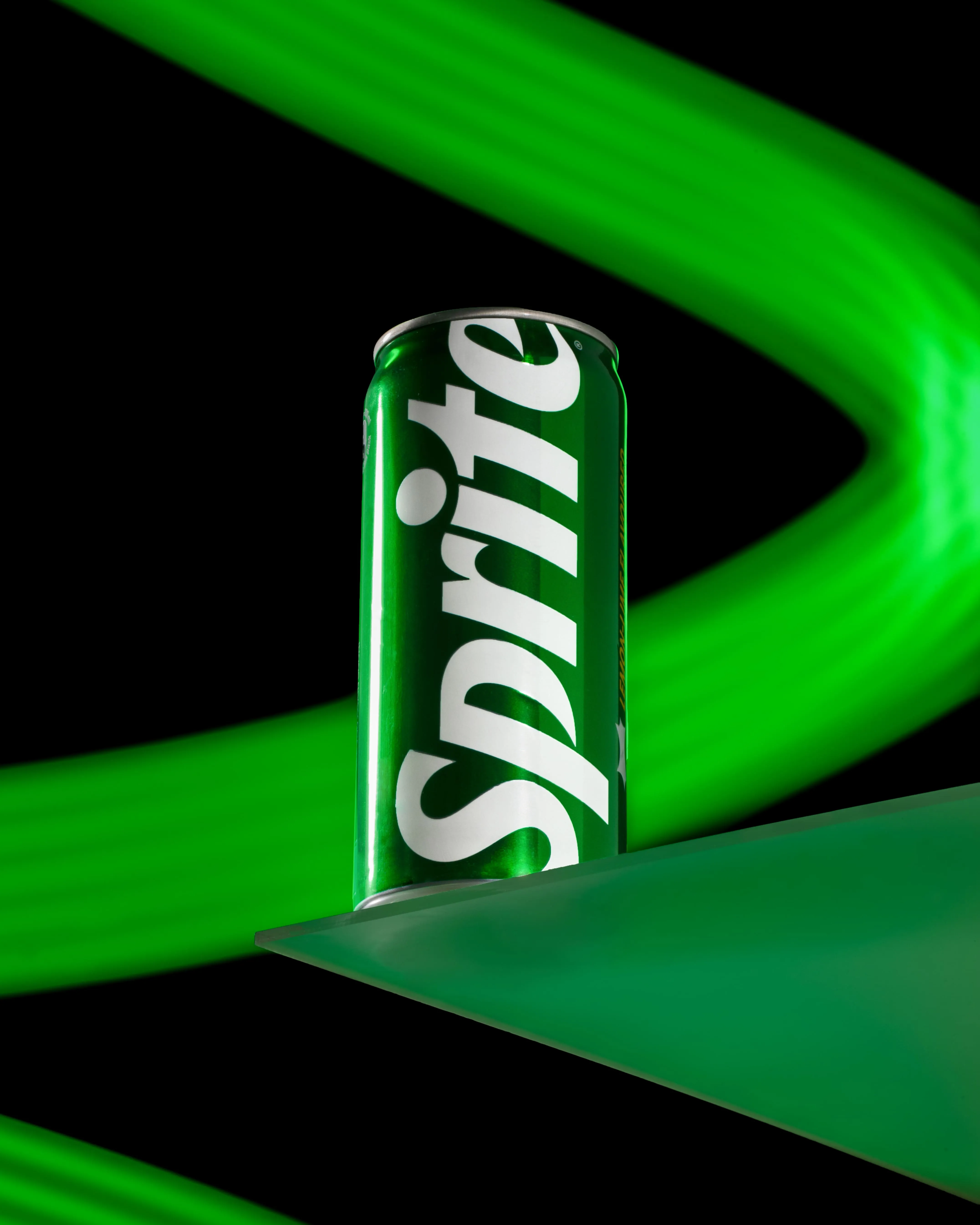 Green can of Sprite soda on a green reflective surface with green light streaks on a black background.