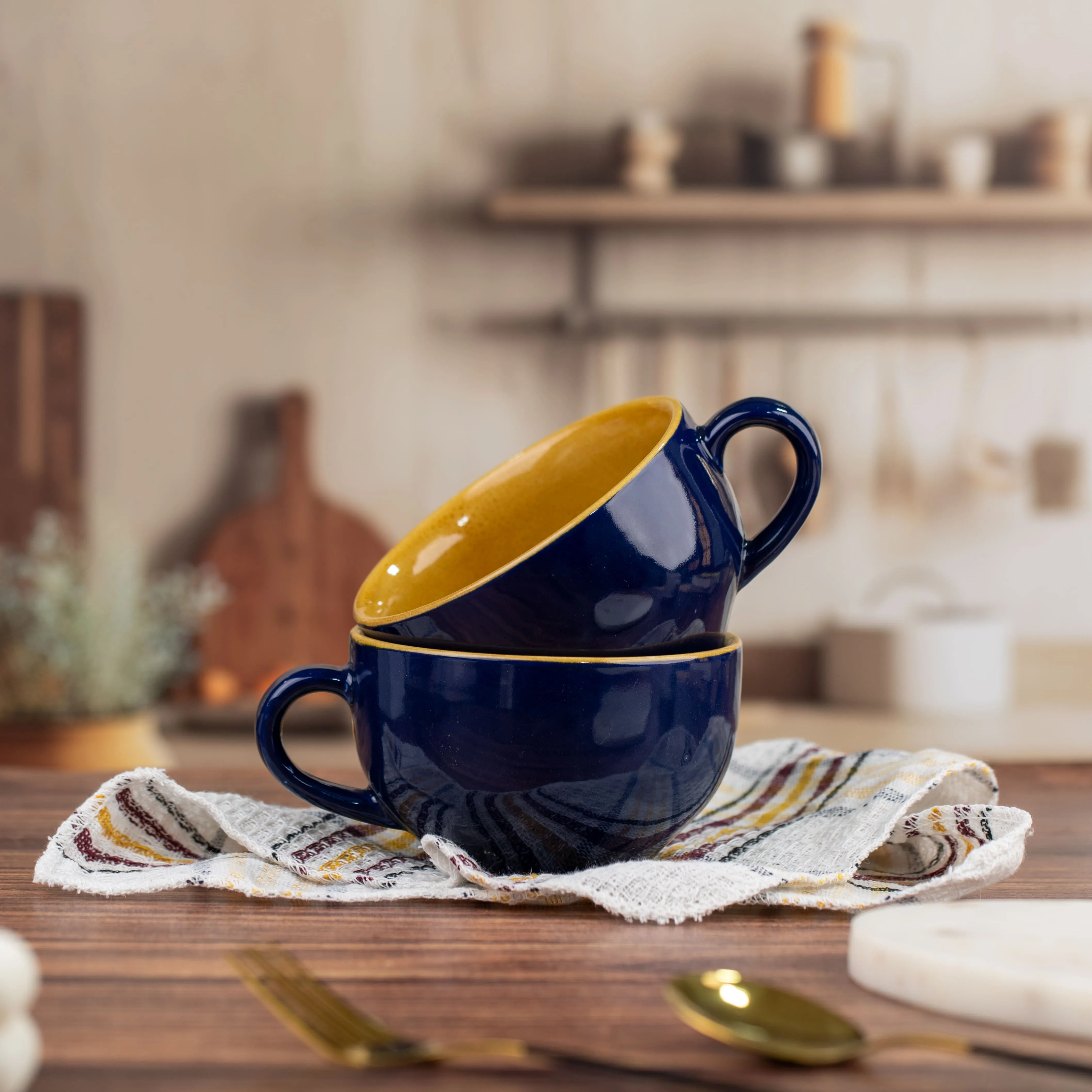 Two dark blue ceramic mugs with yellow interiors stacked on a striped kitchen towel on a wooden countertop.