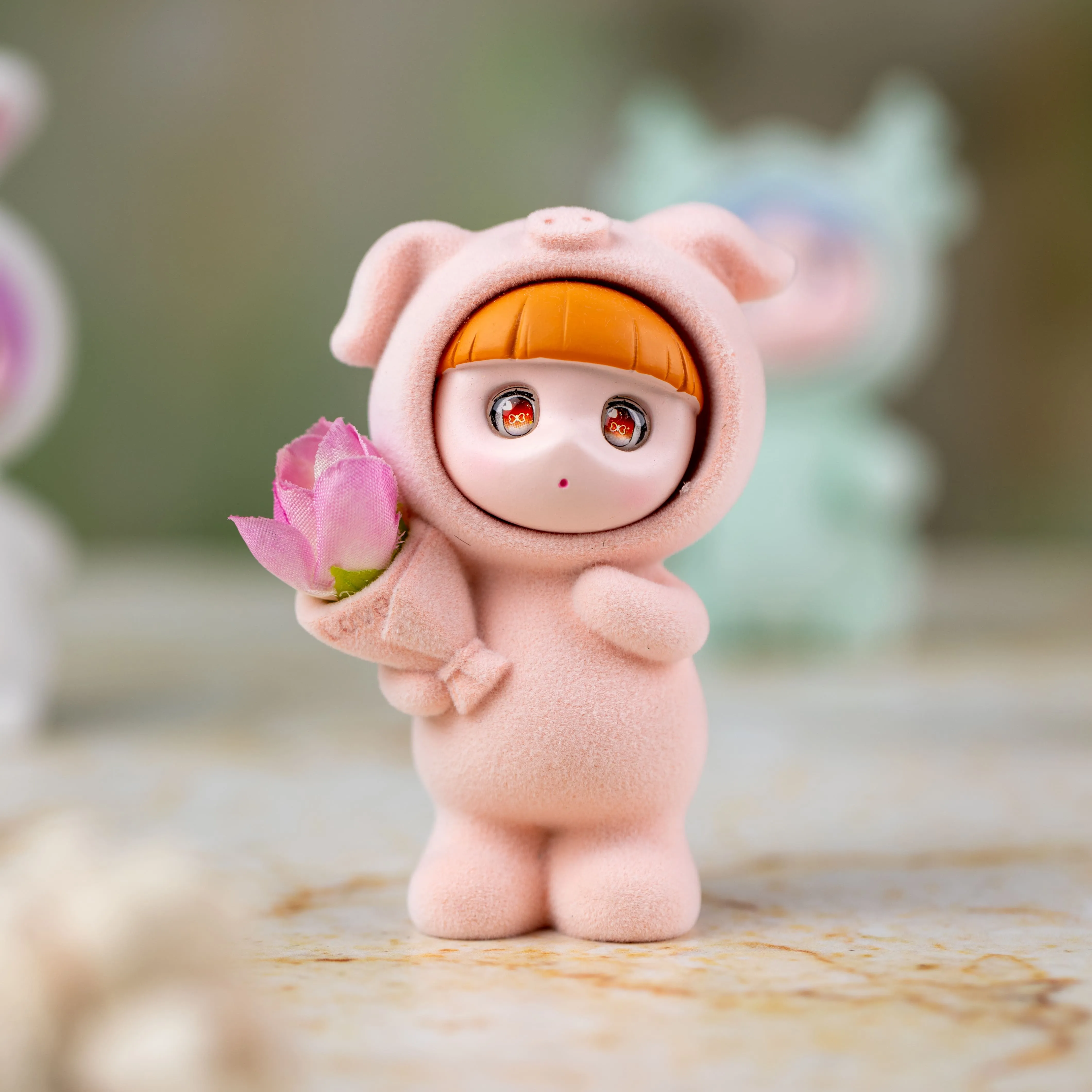 Small figurine dressed in a pink pig costume holding a pink flower bouquet.