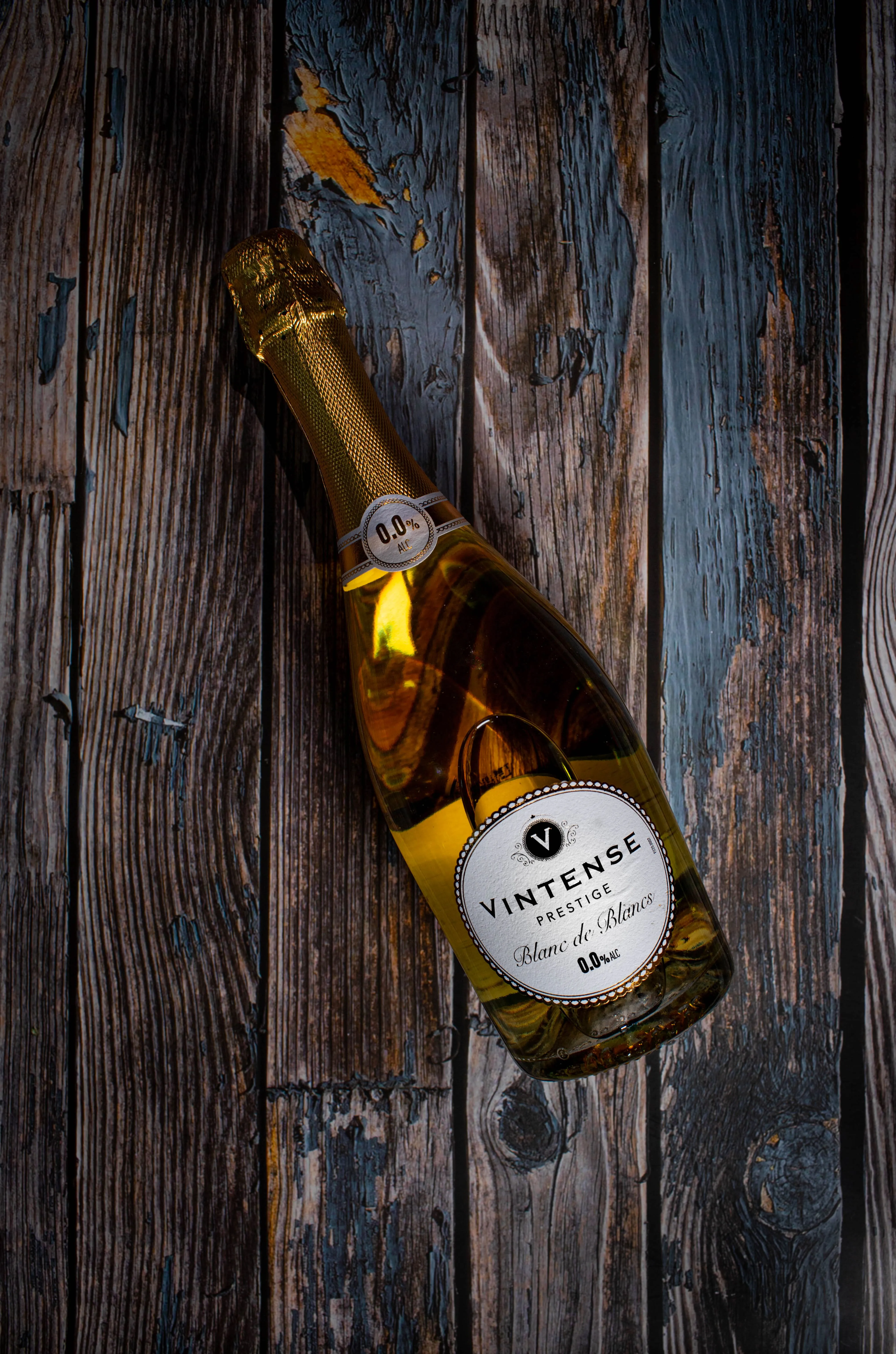 Bottle of Vintense Prestige Blanc de Blancs non-alcoholic sparkling wine on a rustic wooden surface.