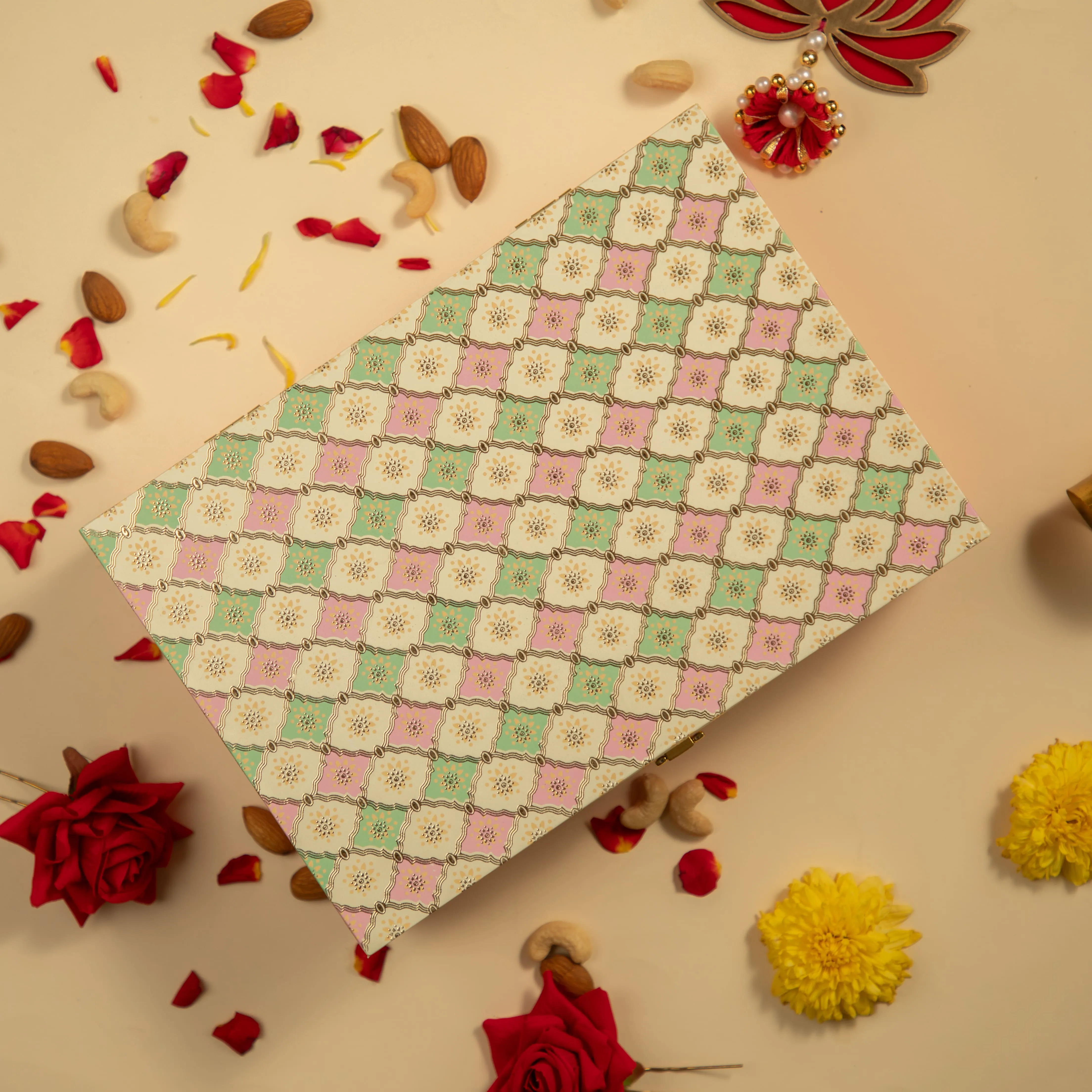 Decorative box with a patterned cover surrounded by rose petals, scattered nuts, red roses, and yellow flowers on a beige surface.