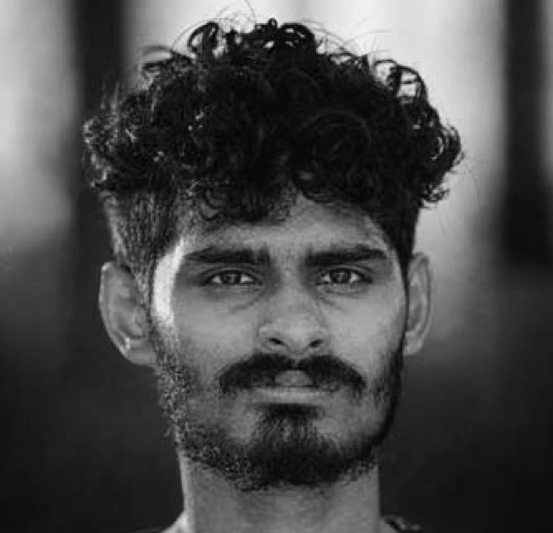 Black and white close-up portrait of a man with curly hair and a beard looking directly at the camera.