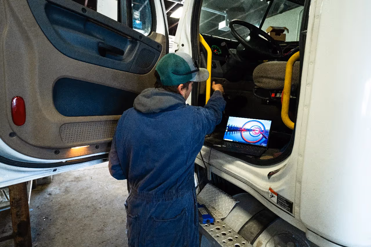 Technician runs electrical diagnostics on a laptop connected to a heavy-duty truck's onboard system.