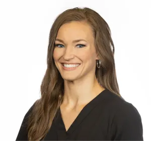 Smiling woman with long brown hair wearing a black top and hoop earrings on a white background.