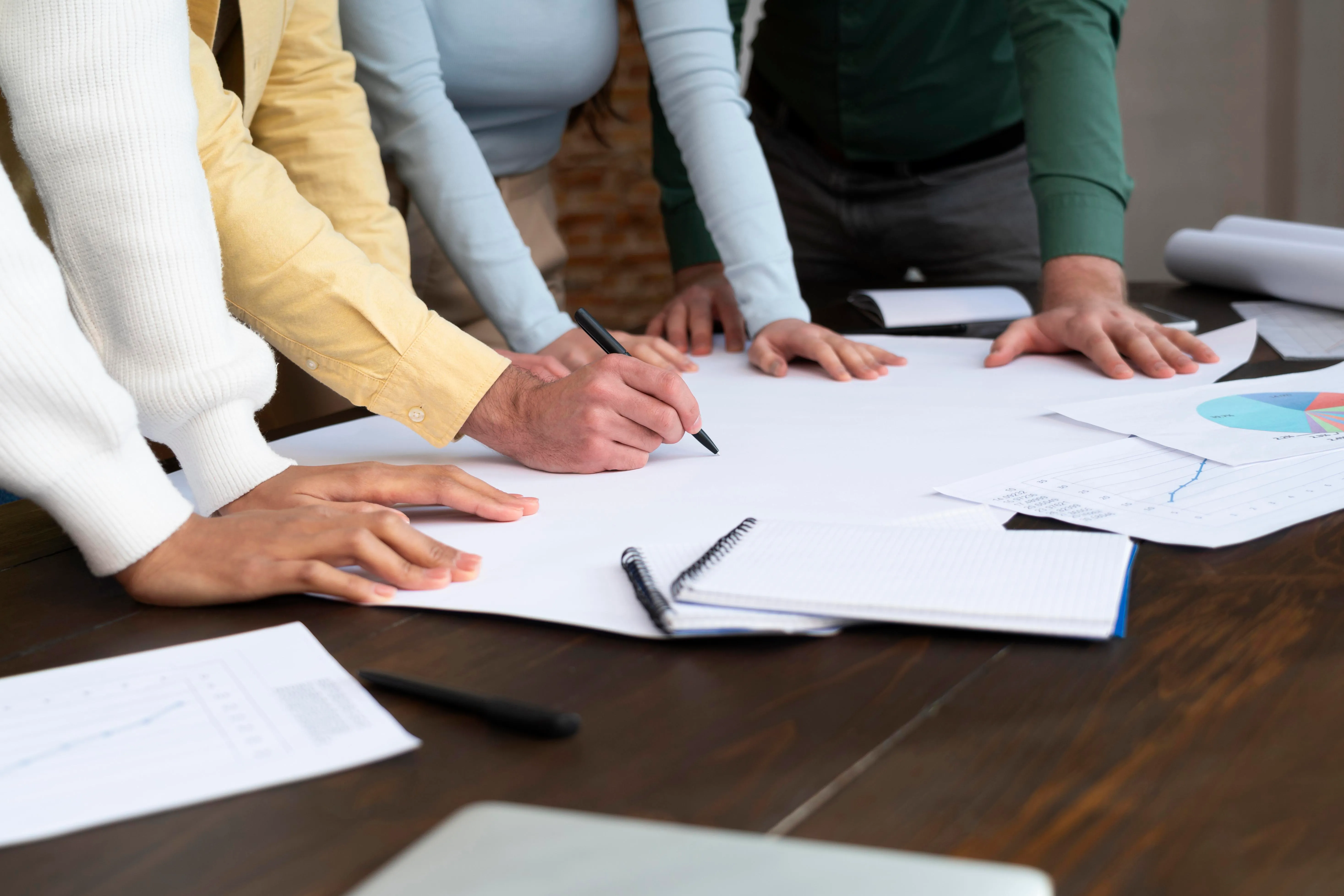Quatre personnes collaborant autour d'une table avec des graphiques et prises de notes, un homme écrit sur un grand papier blanc.