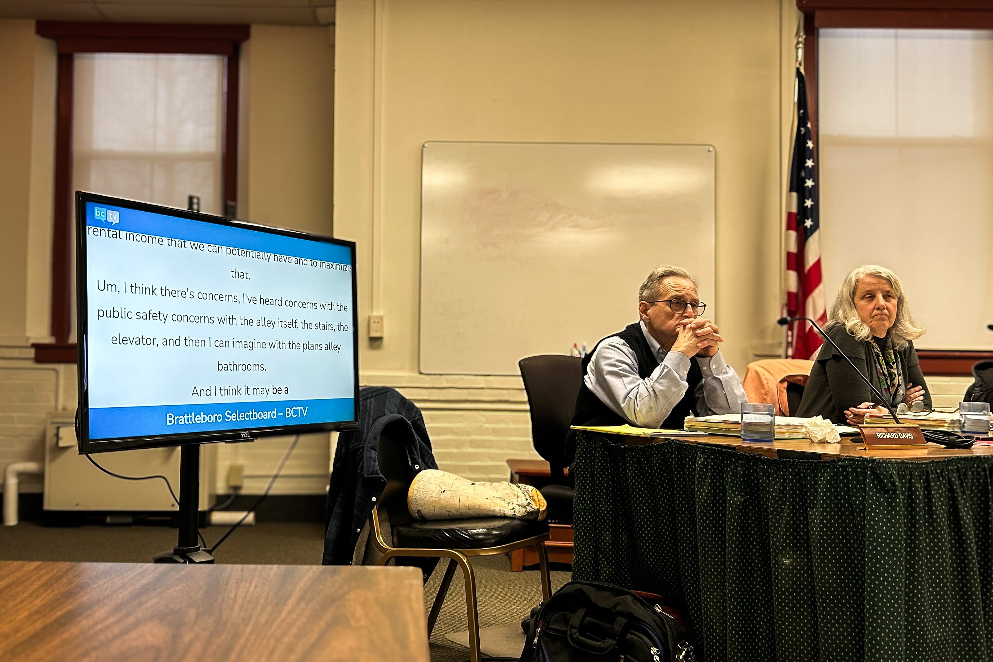 During a Brattleboro city council meeting, live in-room captions powered by MediaScribe are displayed on a screen beside seated board members.