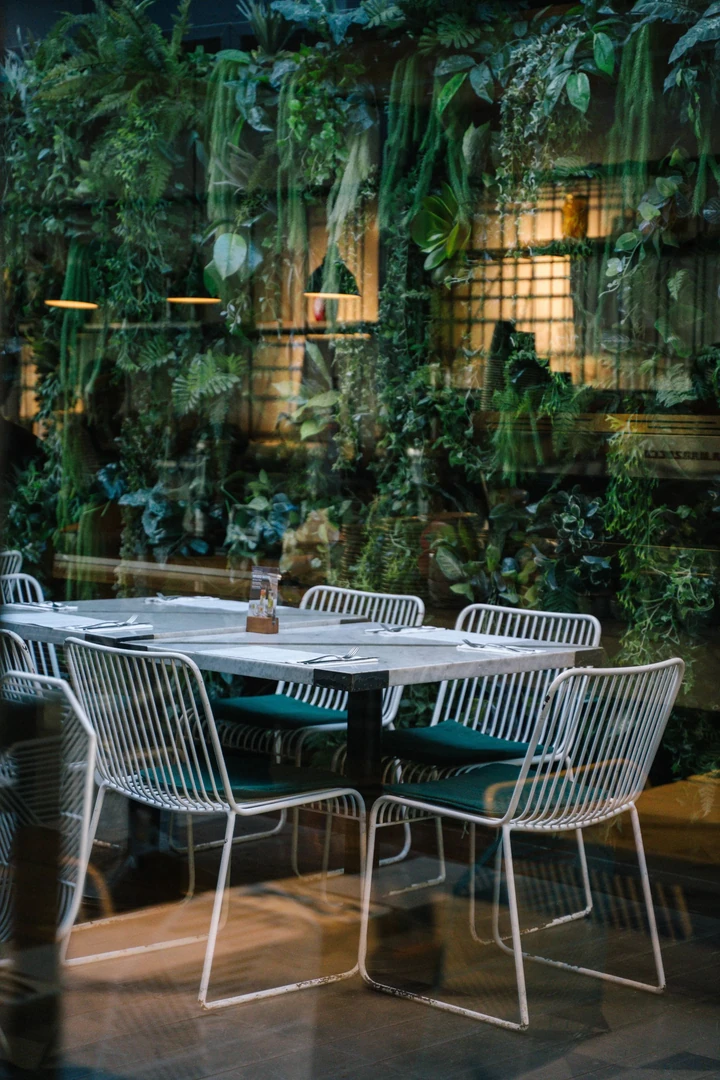 A modern dining table with turquoise and white chairs, set with placemats and cutlery, illuminated by sunlight casting geometric shadows.