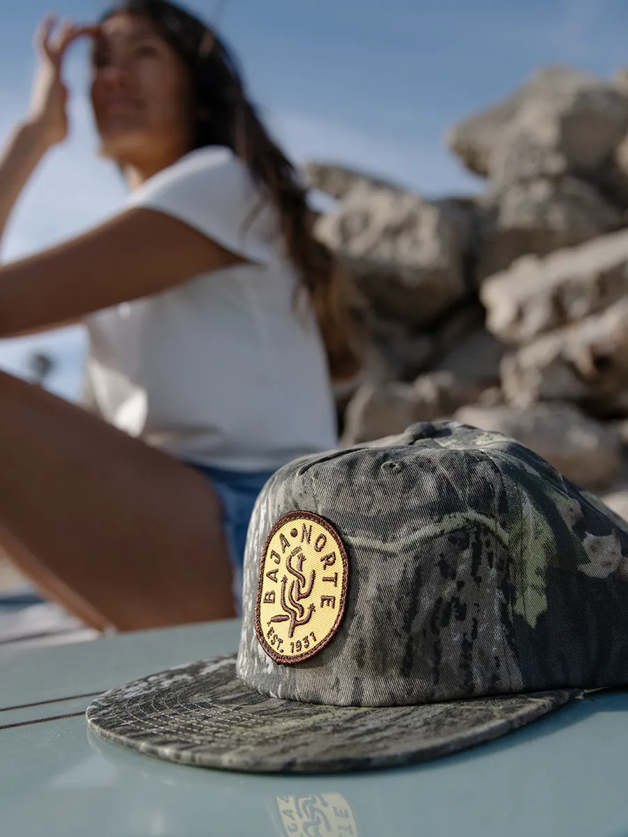 Baja Norte, Mexico hat sitting on surfboard at beach.