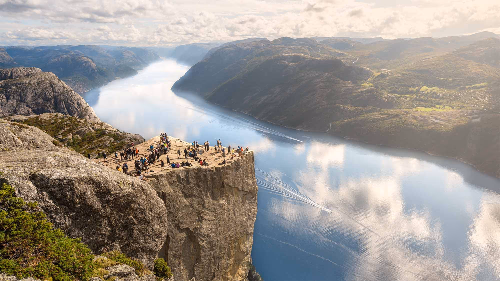 RIB boat full of tourists cruising near a majestic waterfall in the Lysefjord, Norway