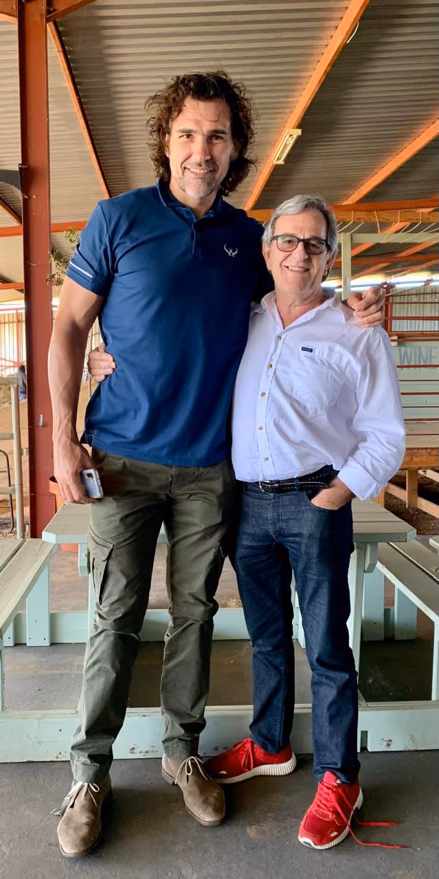Two men smiling with arms around each other in a covered outdoor area with benches.