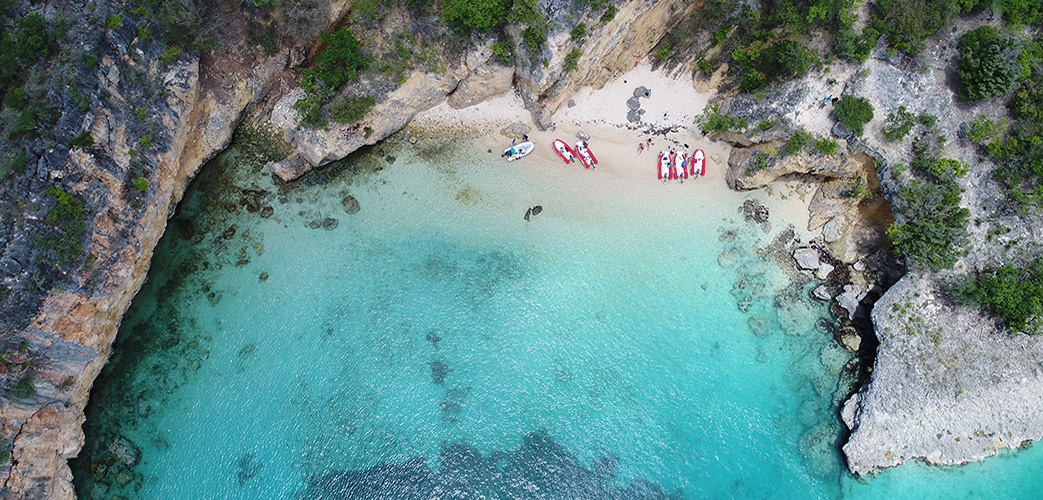 Vue aérienne d’une petite plage isolée aux Caraïbes avec eau turquoise, falaises rocheuses et kayaks rouges sur le sable