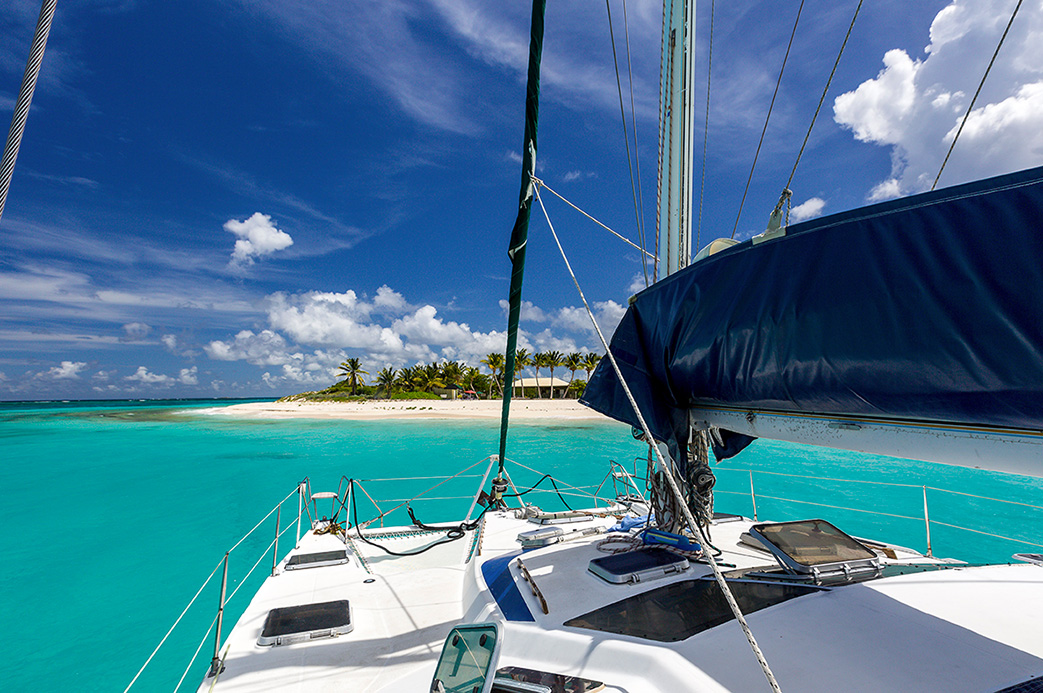 Vue depuis un voilier naviguant dans une eau turquoise vers une plage paradisiaque bordée de palmiers aux Caraïbes