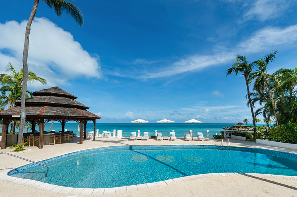Piscine d’un hôtel de luxe à Antigua avec transats, parasols et vue sur la mer turquoise des Caraïbes