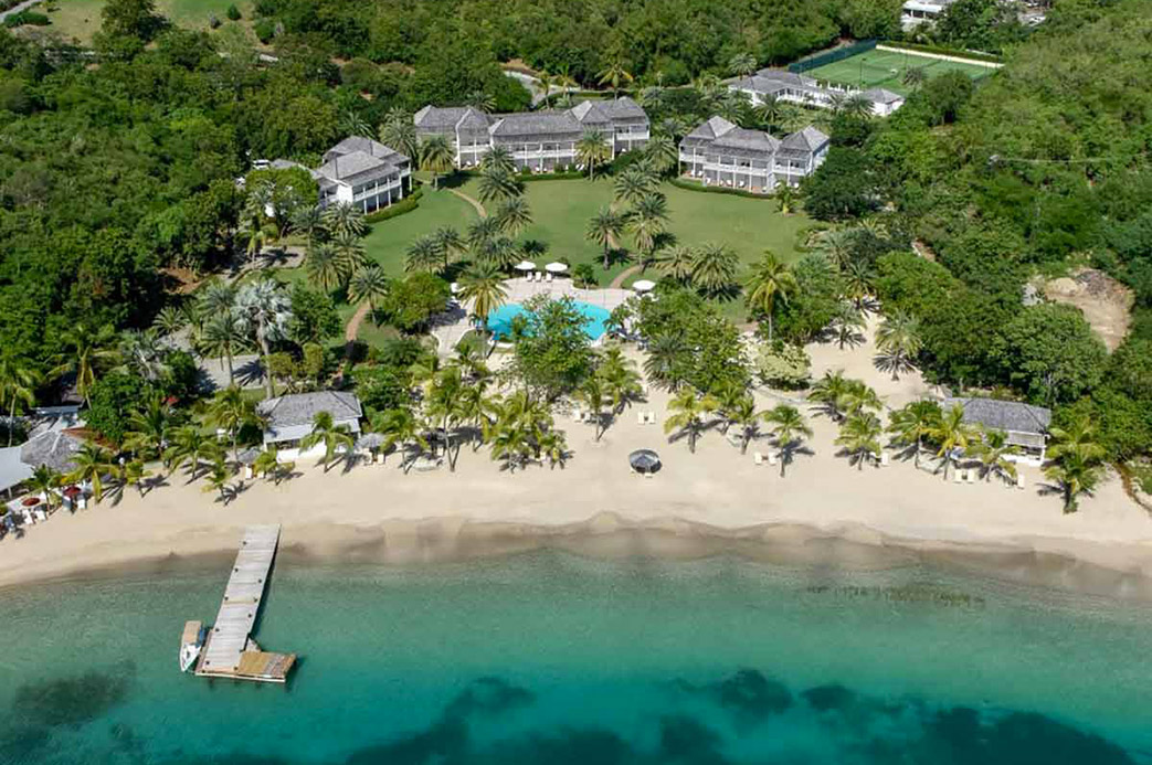 Vue aérienne d’un hôtel en bord de mer à Antigua avec plage de sable fin, piscine, palmiers et jetée privée