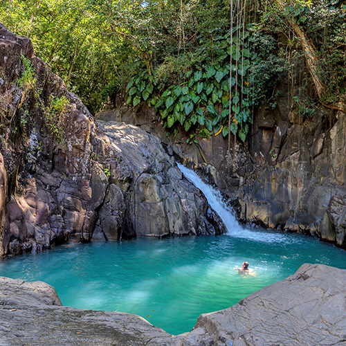 A man swims in a natural rock pool, surrounded by clear, sparkling water.