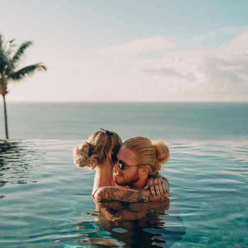 Un homme et une femme s'enlacent dans une piscine à débordement avec vue sur la mer.