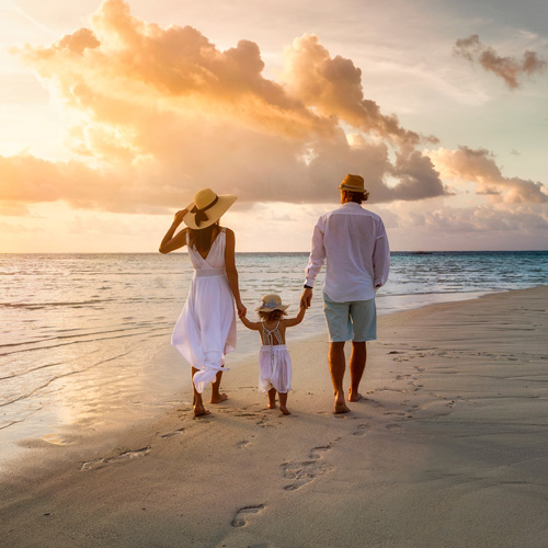 Une famille se promenant sur la plage au coucher du soleil, avec des couleurs chaudes illuminant le ciel.