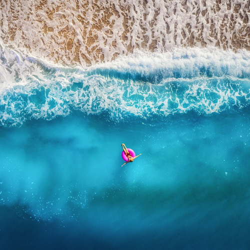 Vue aérienne d'une personne allongée sur une bouée rose flottant au bord de la mer.