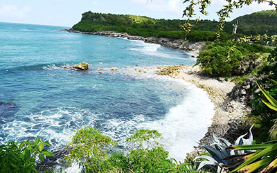 Perspective de l'océan depuis une hauteur, offrant une vue dégagée sur les eaux scintillantes, une plage de galets noirs et le ciel.
