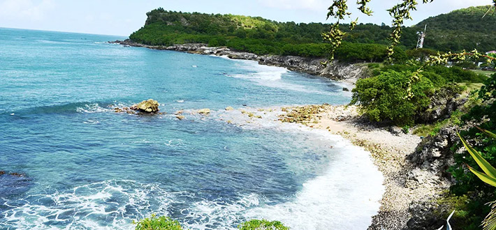 Perspective de l'océan depuis une hauteur, offrant une vue dégagée sur les eaux scintillantes, une plage de galets noirs et le ciel.