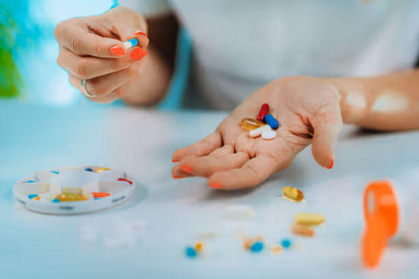 Person holding assorted pills with a weekly medication organizer on the table.
