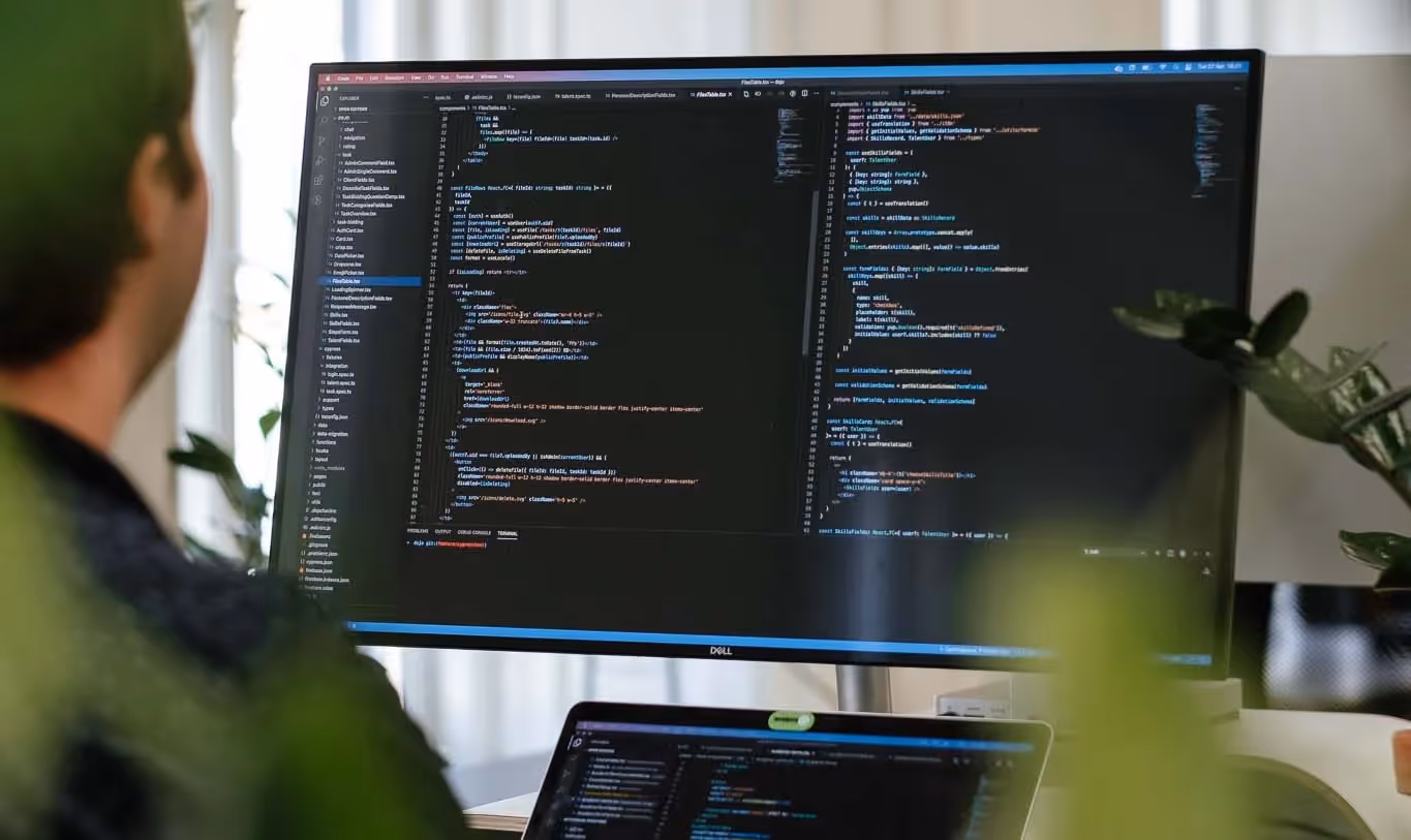 Person working at a desk with code on a monitor.
