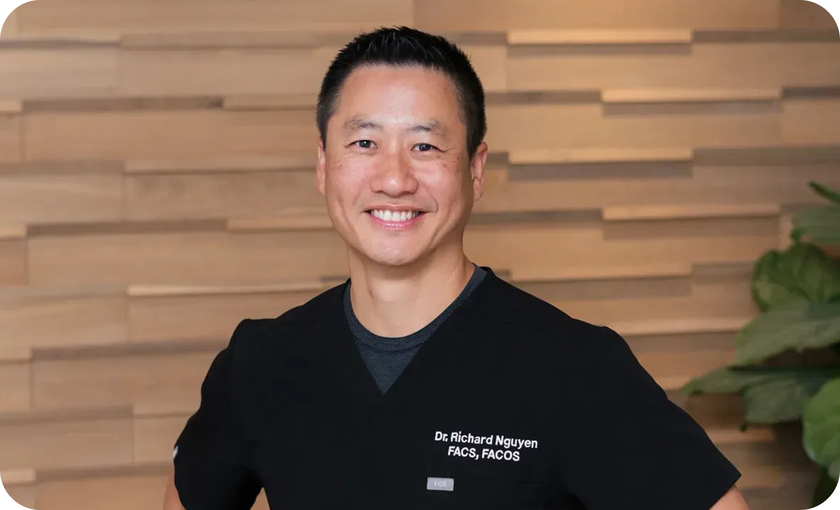 Smiling man wearing black medical scrubs with Dr. Richard Nguyen FACS, FACOS embroidered.