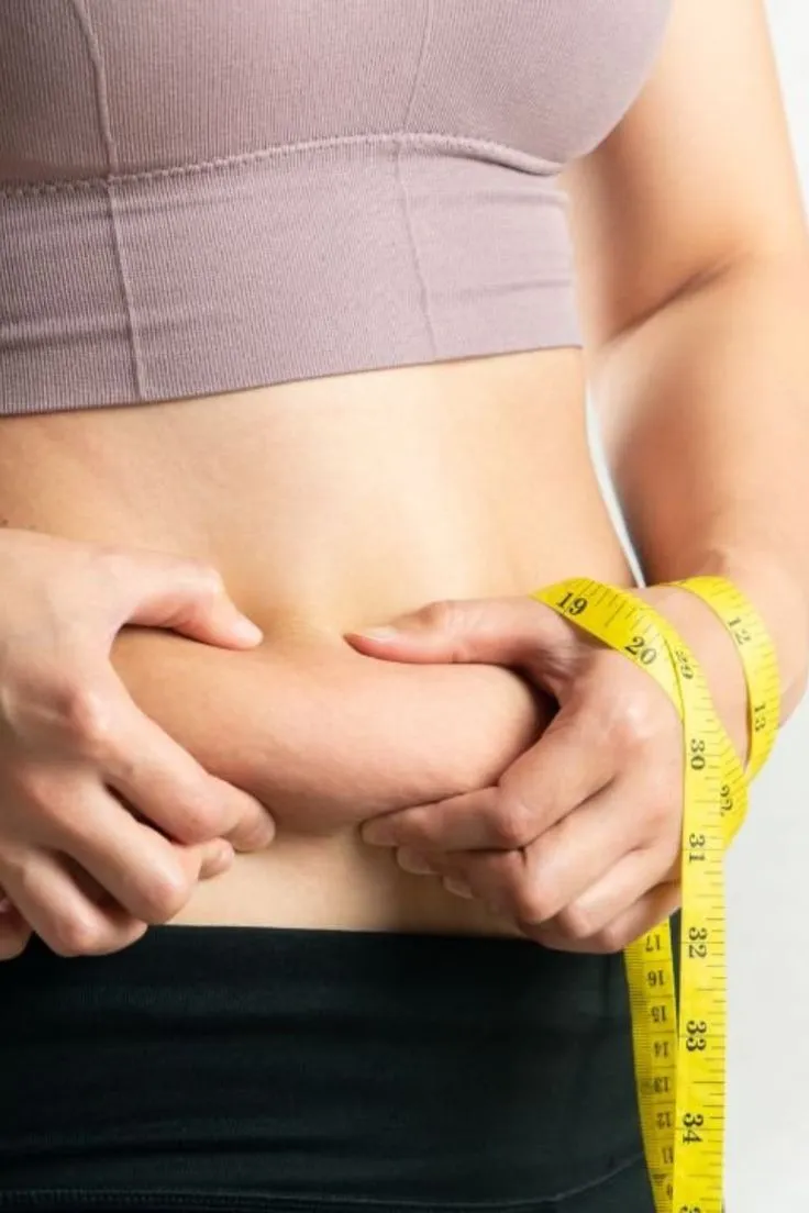 Person pinching belly fat with a yellow measuring tape wrapped around their waist.