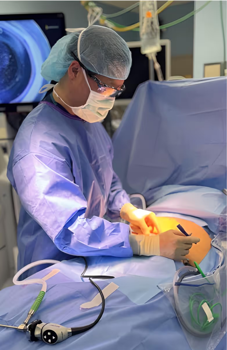 Surgeon in protective gear performing laparoscopic surgery on a patient in an operating room.
