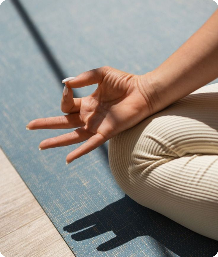 Hand forming a meditation mudra resting on a knee over a blue yoga mat.
