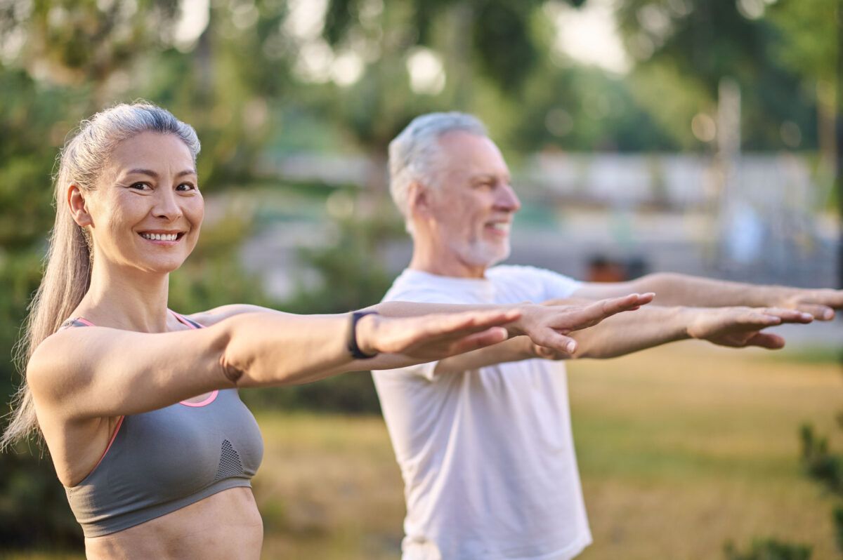 Smiling mature woman and man outdoors stretching arms forward during exercise.