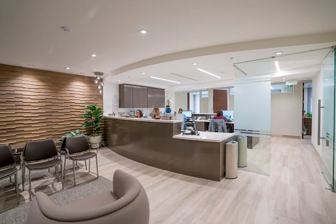 Modern reception area with wooden textured wall, seating, and staff at curved front desk.